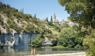 Dos personas junto al río en las cercanías de Saint Martin d’Ardèche, con acantilados y una iglesia al fondo.