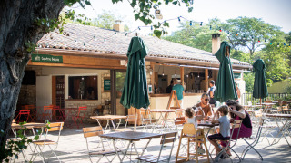 Cafetería al aire libre en Huttopia le Moulin, un parque vacacional en Auvergne-Rhône-Alpes, Francia, con familias.