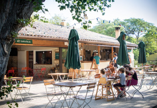 Gezellig buitenterras van Huttopia le Moulin vakantiepark in Auvergne-Rhône-Alpes, met gezinnen aan tafel.