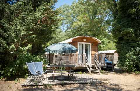 Udendørs foto af en gypsy caravan-hytte ved Huttopia le Moulin i Frankrig, omgivet af træer og have.