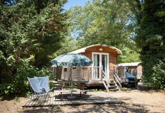 Photo extérieure d'une roulotte à Huttopia le Moulin en France, entourée d'arbres et de verdure.