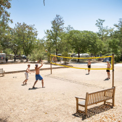 Personas juegan voleibol en un camping de Huttopia le Moulin, rodeados de árboles y casas rodantes.