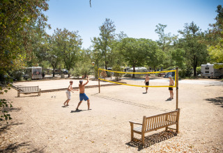 Mensen spelen volleybal op een vakantiepark in Huttopia le Moulin, omgeven door bomen en mobilhomes.