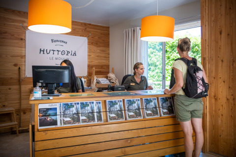 Recepcionista atendiendo a una huésped en el mostrador en Huttopia le Moulin, parque de vacaciones en Auvergne-Rhône-Alpes, Francia.