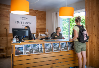 Receptioniste helpt een gast aan de balie bij Huttopia le Moulin vakantiepark in Auvergne-Rhône-Alpes, Frankrijk.