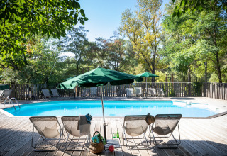 Udendørs swimmingpool med liggestole og grønne parasoller omgivet af træer ved Huttopia le Moulin i Frankrig.