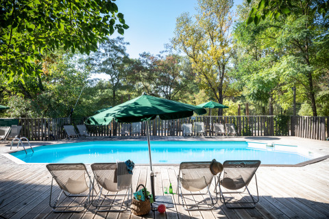 Piscine extérieure avec transats et parasols verts entourée d’arbres à Huttopia le Moulin, en France.