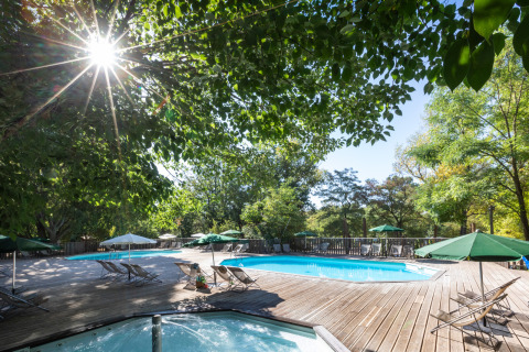 Zona de piscina exterior en Huttopia le Moulin, parque vacacional en Auvergne-Rhône-Alpes, Francia, entre árboles.