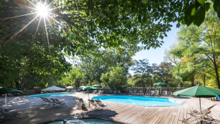Zona de piscina exterior en Huttopia le Moulin, parque vacacional en Auvergne-Rhône-Alpes, Francia, entre árboles.
