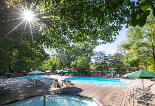 Zona de piscina exterior en Huttopia le Moulin, parque vacacional en Auvergne-Rhône-Alpes, Francia, entre árboles.