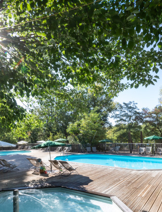 Zona de piscina exterior en Huttopia le Moulin, parque vacacional en Auvergne-Rhône-Alpes, Francia, entre árboles.
