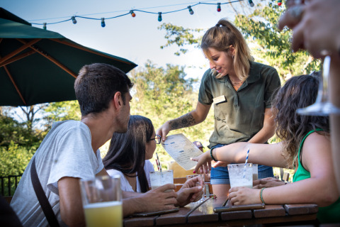 Una camarera toma el pedido de un grupo que disfruta bebidas al aire libre en Huttopia le Moulin en Francia.