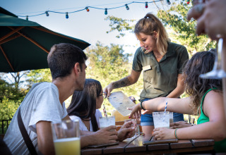 Une serveuse prend la commande d’un groupe profitant de boissons en plein air à Huttopia le Moulin, France.