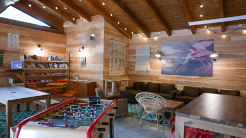 Cozy lounge at Huttopia le Moulin featuring foosball, comfortable sofas, bookshelves, and rustic decor.