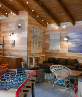 Acogedora sala común en Huttopia le Moulin con futbolín, sofás, libros y decoración de madera clara.