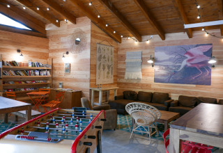 Cozy lounge at Huttopia le Moulin featuring foosball, comfortable sofas, bookshelves, and rustic decor.