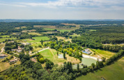 Luftfoto af Huttopia Vallée du Lot feriepark i Nouvelle-Aquitaine, Frankrig, omringet af grønt landskab.