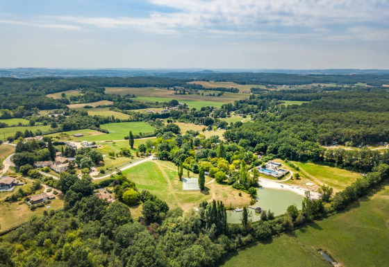 Luftfoto af Huttopia Vallée du Lot feriepark i Nouvelle-Aquitaine, Frankrig, omringet af grønt landskab.