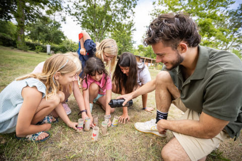 Kinder und ein Erwachsener spielen mit bunten Pappröhren auf dem Rasen im Huttopia Vallée du Lot, Frankreich.