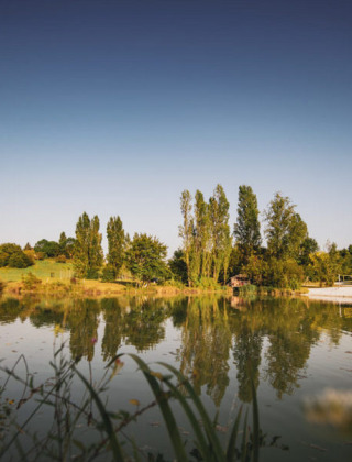 Paisaje sereno junto a un lago cerca de St. Étienne-de-Villeréal, Nouvelle-Aquitaine, Francia, con árboles y agua tranquila.