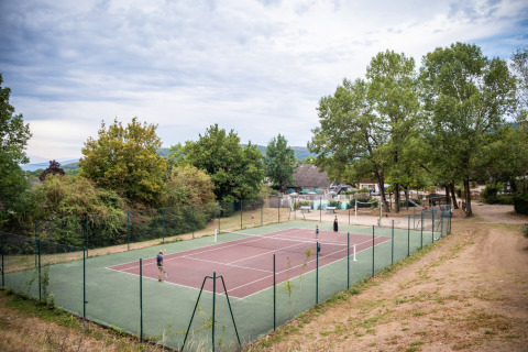 Pista de tenis con jugadores rodeada de árboles en Huttopia Divonne Les Bains, Auvergne-Rhône-Alpes, Francia.
