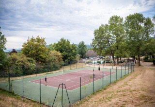 Tennisveld met spelers omringd door bomen in Huttopia Divonne Les Bains, Auvergne-Rhône-Alpes, Frankrijk.