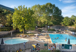 Piscine extérieure au Huttopia Divonne Les Bains avec des familles et des enfants entourés d’arbres en France.