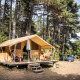 To personer slapper af udenfor et Toile&bois safari telt Classic i en skovrig campingplads atmosphere.