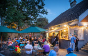 Udendørs restaurant på Huttopia Divonne Les Bains med folk, der nyder aftenen under grønne parasoller.
