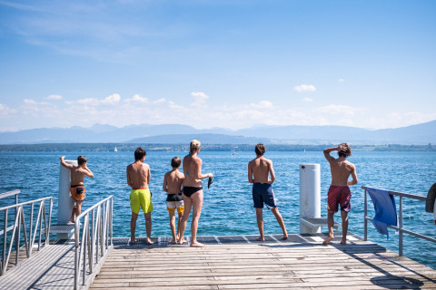 Des jeunes profitent du soleil sur un ponton au bord du lac à Huttopia Divonne Les Bains, en Auvergne-Rhône-Alpes.