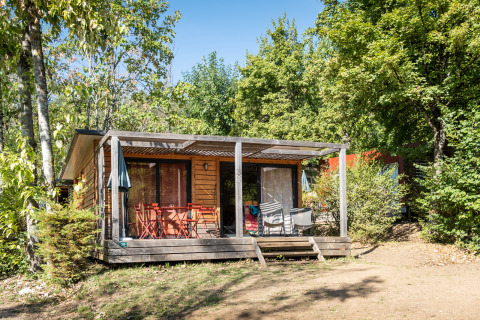 Houten bungalow met overdekt terras in het groen bij Huttopia Divonne Les Bains, Frankrijk.
