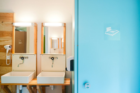 Bagno moderno con due lavandini, specchi e porta blu presso Huttopia Divonne Les Bains, Francia.
