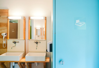 Moderne badkamer met twee lavabo's, spiegels en een blauwe deur in Huttopia Divonne Les Bains, Frankrijk.