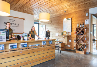 Receptie van Huttopia Divonne Les Bains met twee medewerkers, houten wanden en wijnrek in Frankrijk.