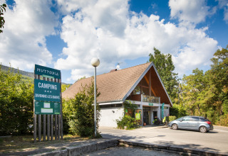 Toegang tot camping Huttopia Divonne Les Bains in Auvergne-Rhône-Alpes, Frankrijk onder een blauwe lucht.