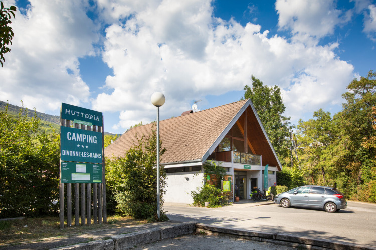 Entrance of Huttopia Divonne Les Bains holiday park in Auvergne-Rhône-Alpes, France, with blue sky.