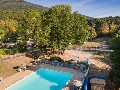 Piscina al aire libre y cancha de tenis rodeadas de naturaleza en Huttopia Divonne Les Bains, Auvergne-Rhône-Alpes, Francia.