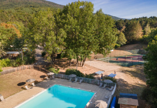 Buitenzwembad en tennisveld omgeven door natuur bij Huttopia Divonne Les Bains, Auvergne-Rhône-Alpes, Frankrijk.