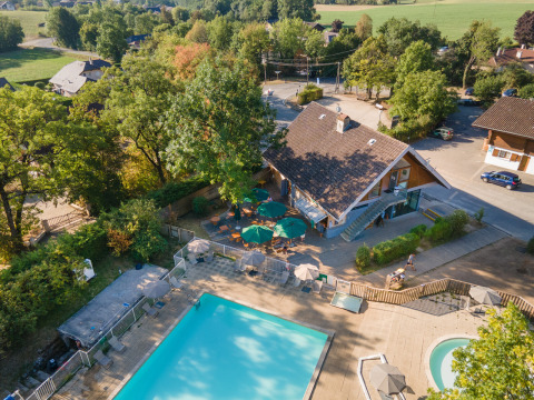 Vista aérea del parque vacacional Huttopia Divonne Les Bains en Auvergne-Rhône-Alpes con piscina y árboles.