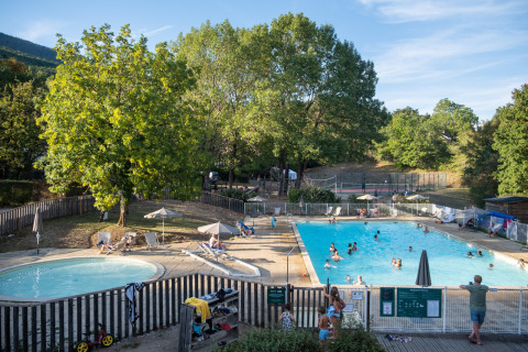 Piscine extérieure et pataugeoire entourées d’arbres à Huttopia Divonne Les Bains, en France.