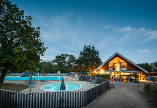 Avondbeeld van Huttopia Divonne Les Bains vakantiepark met zwembad en verlicht hoofdgebouw in Frankrijk.