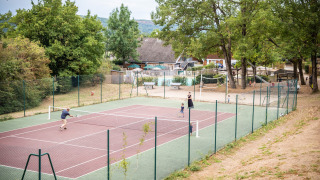 Personas jugando tenis en una cancha al aire libre en Huttopia Divonne Les Bains en Auvergne-Rhône-Alpes.
