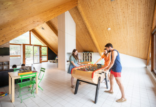 Indoor lounge at Huttopia Divonne Les Bains, France, with adults playing foosball and relaxing.