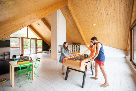 Sala interior en Huttopia Divonne Les Bains, Francia, con adultos jugando futbolín y relajándose.