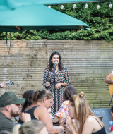 Musiker treten im Freien auf einer Bühne auf, während Besucher im Huttopia Divonne Les Bains essen.