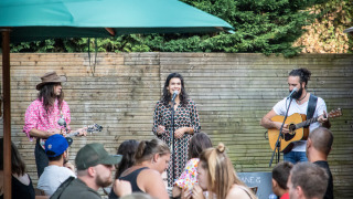 Músicos actúan en el exterior mientras la gente cena en Huttopia Divonne Les Bains, parque de vacaciones.