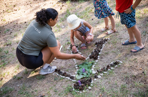 Niños y un adulto crean arte natural con hojas y piedras en Huttopia Divonne Les Bains, Francia.