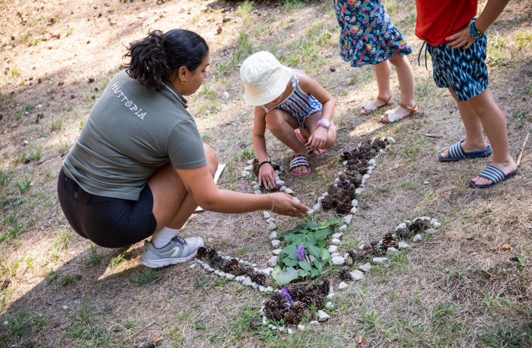 Children and an adult create nature art with leaves and stones at Huttopia Divonne Les Bains, France.