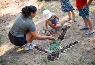 Kinderen en volwassene maken natuuraart met bladeren en stenen bij Huttopia Divonne Les Bains, Frankrijk.