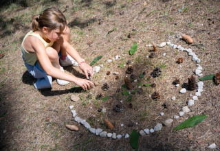 Kind maakt natuurkunst met dennenappels, steentjes en bladeren in Huttopia Divonne Les Bains, Frankrijk.